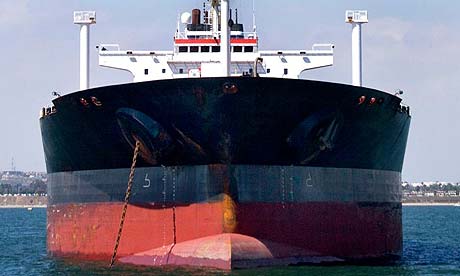 A large cargo ship sits at anchor in the calm waters of a safe harbour