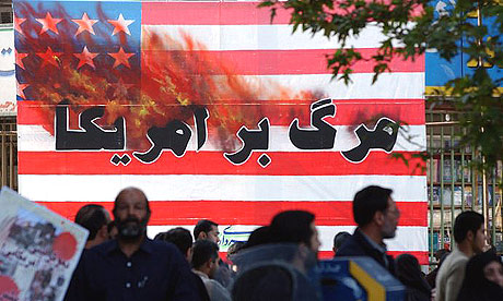 Iranians pass a US flag with a sign reading 